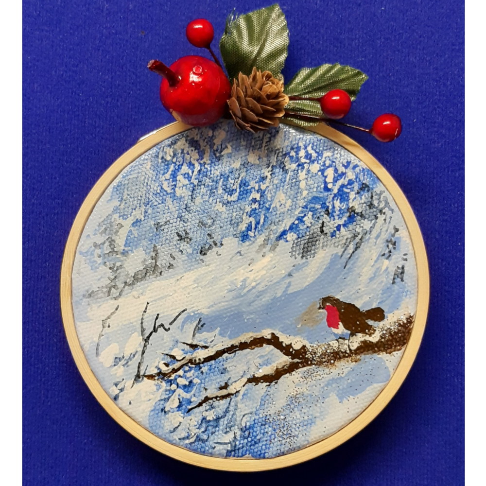 Original signed artwork, Circle Christmas robin canvas decoration. Robin sitting on a snow covered branch to the right looking to the left, with frosty shades of blue background. Sealed with a varnish finish, dusted with a hint of sparkle and added festive trimmings. Framed in a sustainable bamboo hoop ring.