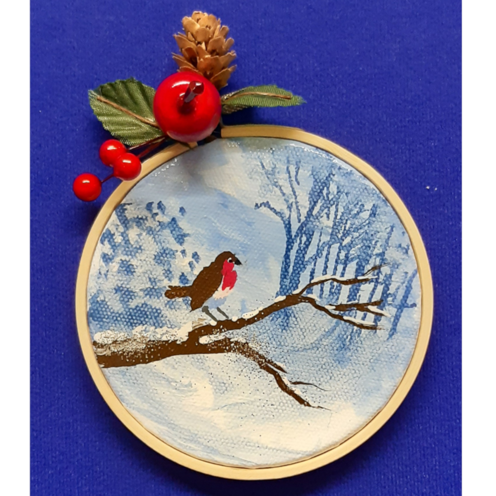 Original signed artwork, Circle Christmas robin canvas decoration. Robin sitting on a snow covered branch to the left looking right, with frosty shades of blue background. Sealed with a varnish finish, dusted with a hint of sparkle and added festive trimmings. Framed in a sustainable bamboo hoop ring.