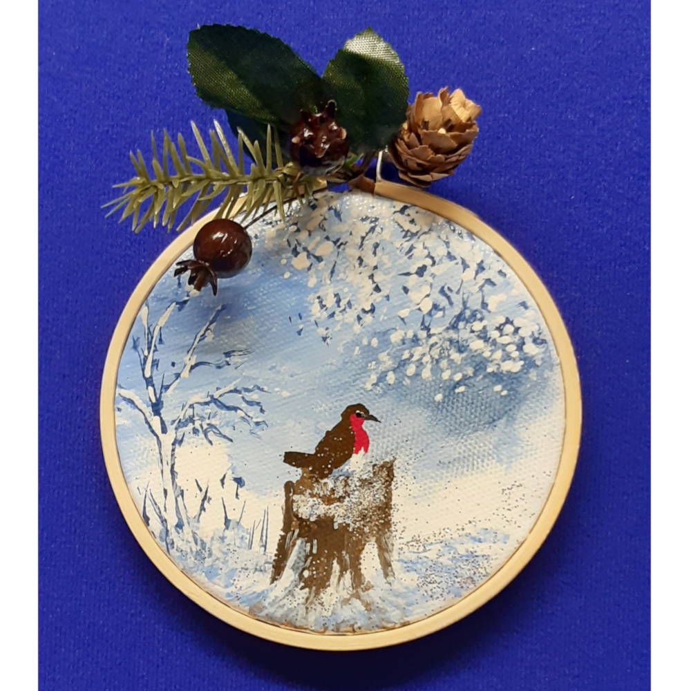 Original signed artwork, Circle Christmas robin canvas decoration. Robin sitting on a snow covered tree stump in the foreground and looking to the right, with frosty shades of blue background. Sealed with a varnish finish, dusted with a hint of sparkle and added festive trimmings. Framed in a sustainable bamboo hoop ring.