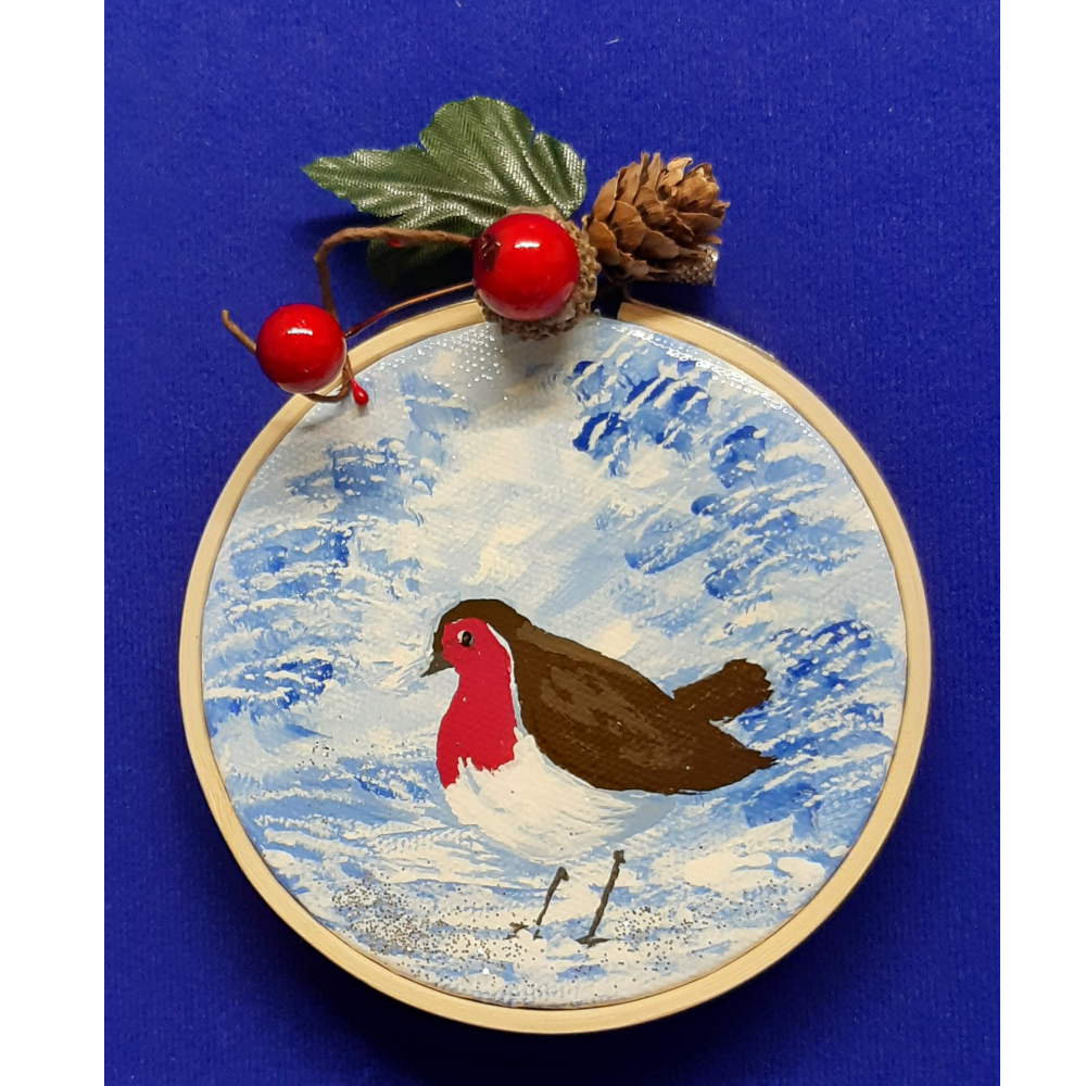 Original signed artwork, Circle Christmas robin canvas decoration. Robin on snow covered ground looking to the left, with frosty shades of blue background. Sealed with a varnish finish, dusted with a hint of sparkle and added festive trimmings. Framed in a sustainable bamboo hoop ring.