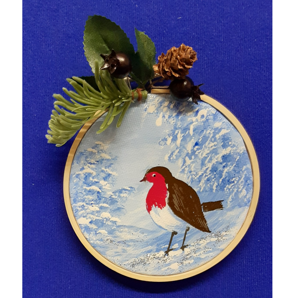 Original signed artwork, Circle Christmas robin canvas decoration. Robin on snow covered ground looking to the left with frosty shades of blue background. Sealed with a varnish finish, dusted with a hint of sparkle and added festive trimmings. Framed in a sustainable bamboo hoop ring.