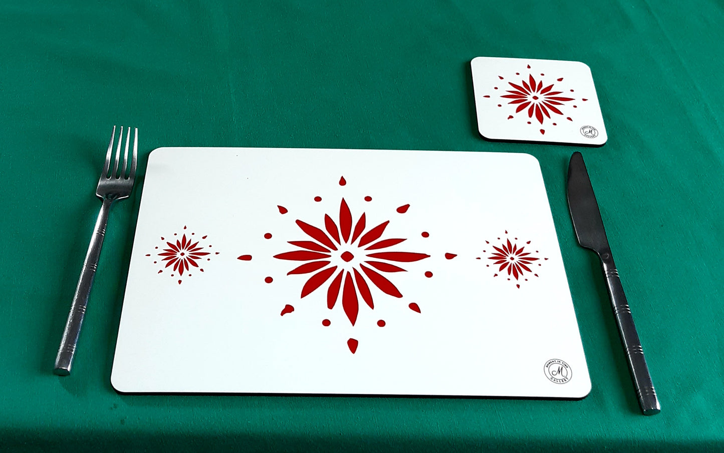 White table mat and coaster set with red flowerburst design. Set up on top of blue table surface. Single table and coaster mat set. Heat resistant place mats.