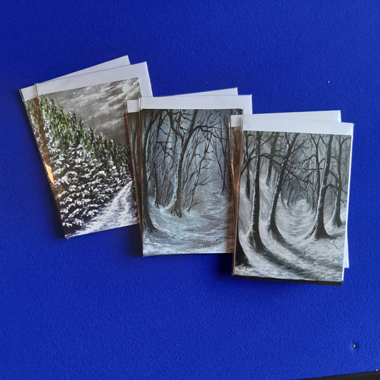 Mix-and-Match-Woodland Walks. A collection of 6 Christmas cards. Three greeting cards featuring two of each, Moonlit Forest Trail, Woodland Walk and Woodland Trail. All set in wnter forest scenes, fanned out on a vibrant blue background.
Size A6 (5"x7") Pack of 6 cards with white envelopes.