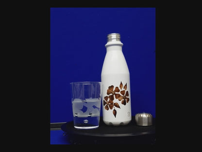 Video of White aluminium water bottle with brown floral design, with a glass sitting next to it on a blue background.   Demontrating the ease of cap attachment. 650 ml Designer bottle.